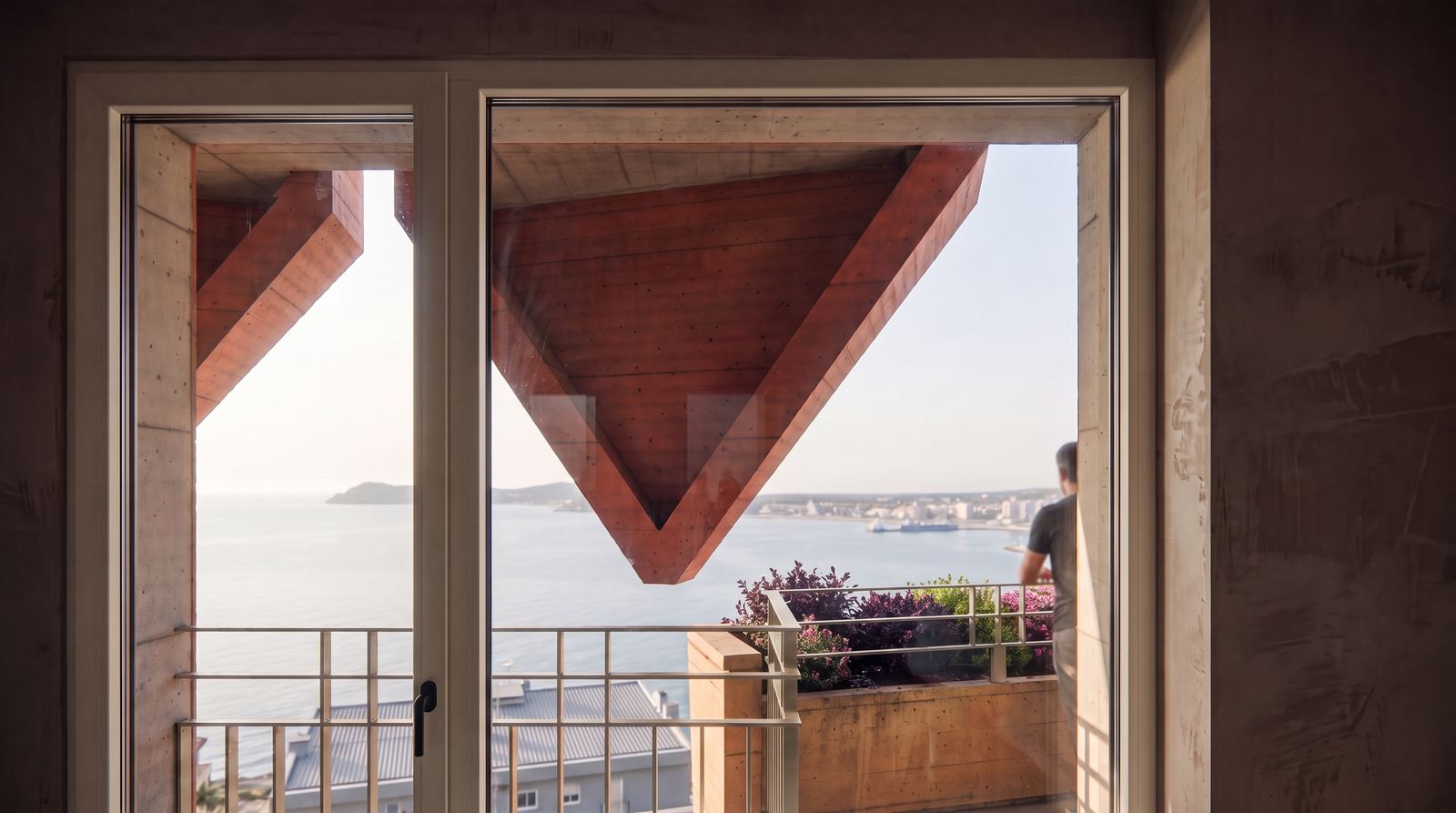 Interior view through floor-to-ceiling glass opening onto a private terrace with inverted red concrete brise-soleil.